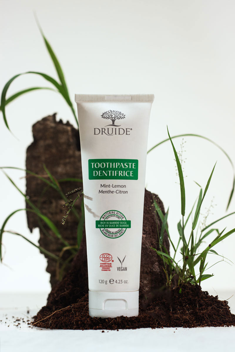 Druide Organic Mint-Lemon Toothpaste, (120 g, 4.23 oz.) the white tube dispenser shown standing against background of natural soil and fresh grass.