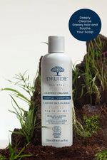 Druide Purity Shampoo white plastic flip top dispenser of 250 ml shown in a natural surrounding against a mound of fresh garden soil and green grass.