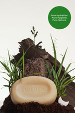 Druide Pur and Pure Natural Soap bar shown against a backdrop of fresh soil and grass with text reading