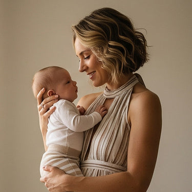 Modern halter top clad British woman holding her baby after using druide biolove baby products standing against beige background.