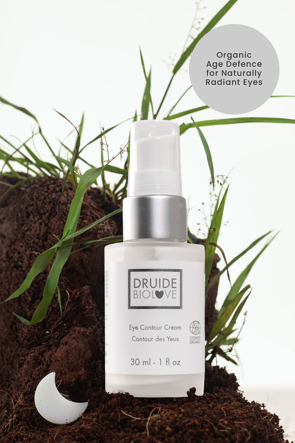 Druide Biolove Organic Eye Contour Cream dispenser shown in natural environment of fresh garden soil and green grass with text reading "organic age defence for naturally radiant eyes".