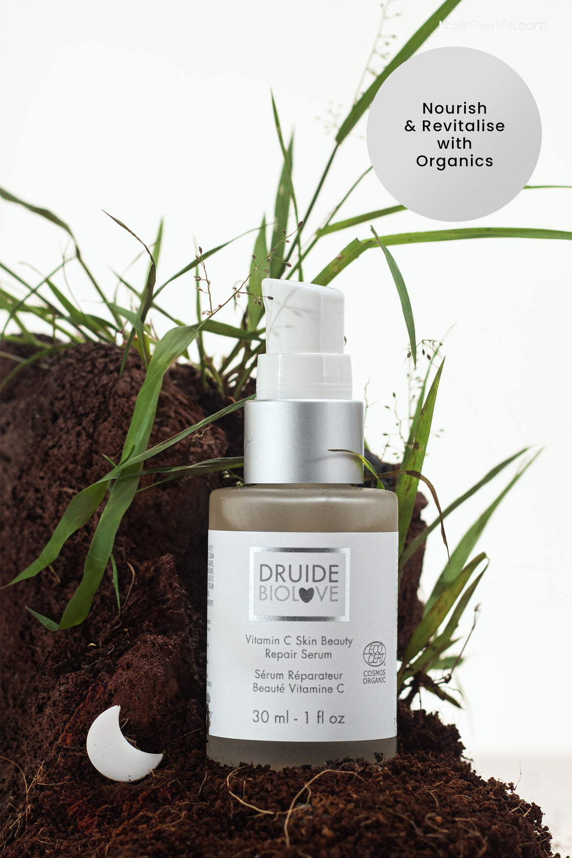 Druide Biolove Vitamin C Serum dispenser shown against a natural background of soil and grass with the text "Nourish & revitalise with organics".