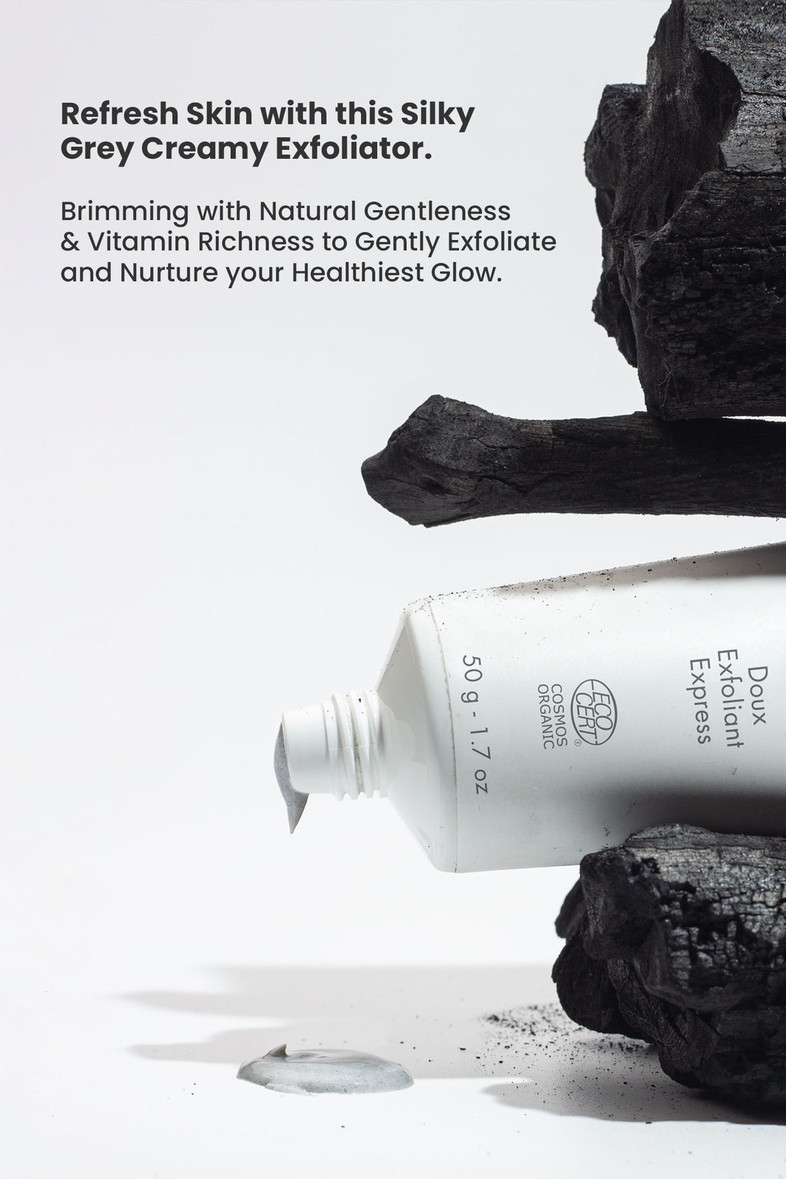 White tube of Druide Biolove Organic Exfoliating Cleanser for Sensitive Skin stacked with charcoal and dispensing creamy exfoliator cream with text stating "refresh skin with this silky grey creamy exfoliator brimming with natural gentleness and vitamin richness to gently exfoliate and nurture your healthiest glow".