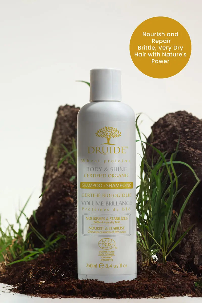 Druide body and shine shampoo for dry brittle hair flip top dispenser of 250 ml shown in natural surroundings of fresh spoil and green grass with text stating "nourish and repair brittle, very dry hair with nature's power".