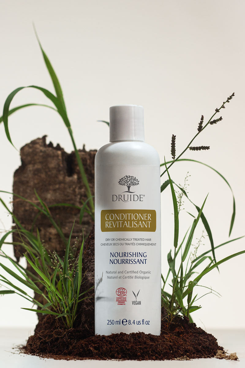 Druide Natural Hair Conditioner dispenser shown in a natural environment with fresh soil and green grass in background.