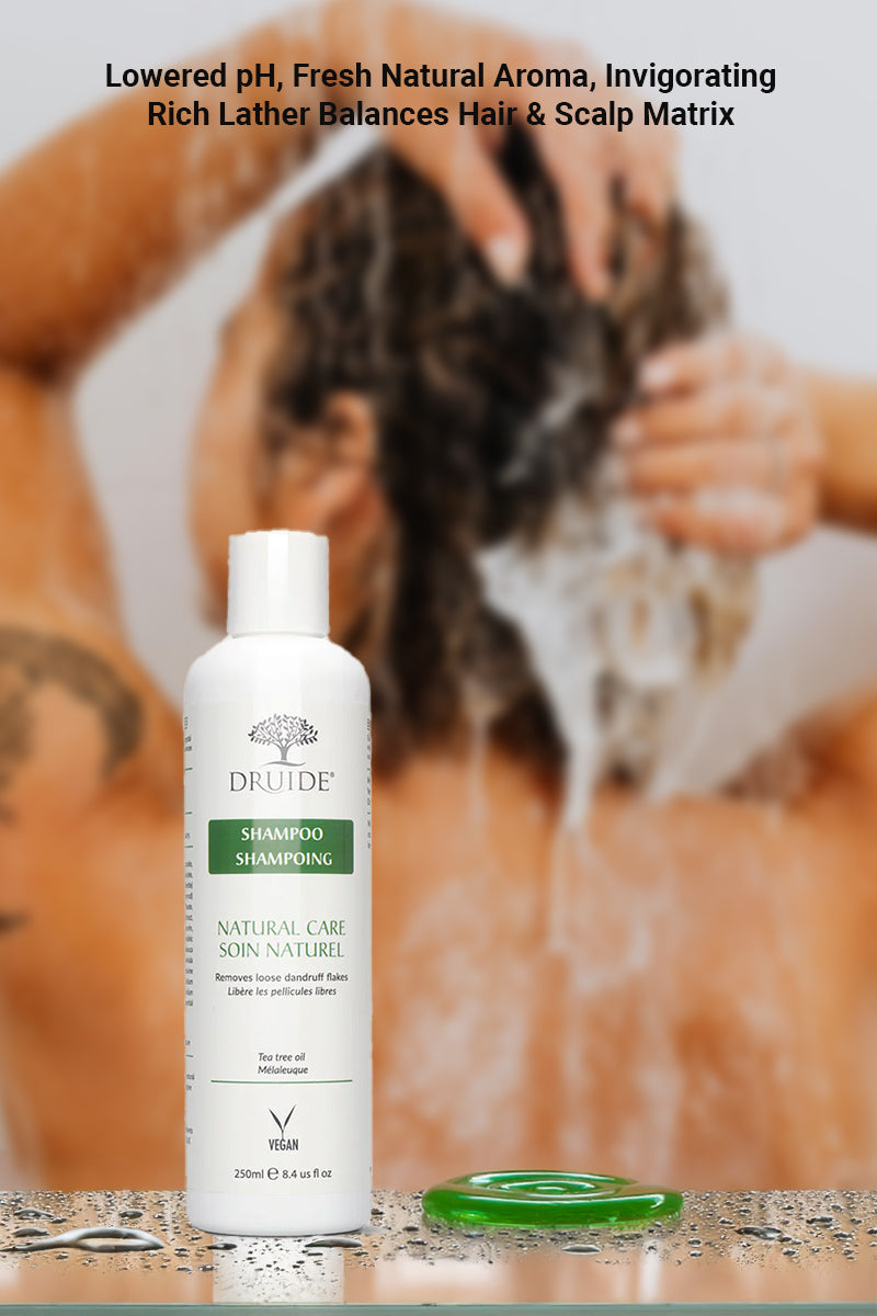 Druide Tea Tree Oil Shampoo dispenser and some light green shampoo squeezed out shown against the backdrop of a woman washing her hair with lather, and text reading "lowered pH, fresh natural aroma, invigorating rich lather balances hair and scalp matrix".