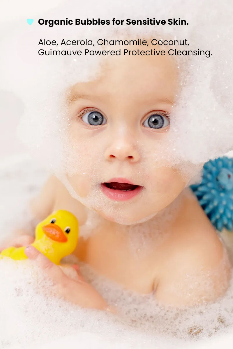 toddler in a bath immersed in rich foam and playing with a yellow rubber duck, text displaying "organic bubbles for sensitive skin".