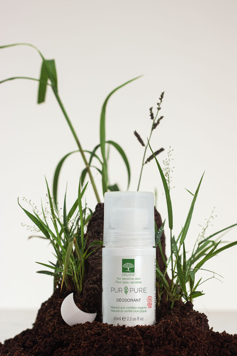 Druide Pur&Pure Natural Deodorant dispenser against a background of fresh soil and green grass.