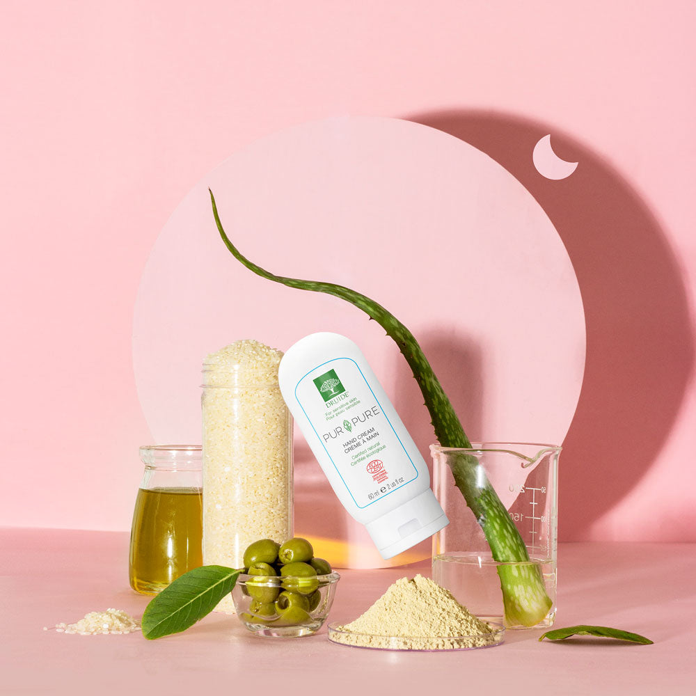 Druide Pur and Pure organic hand cream dispenser surrounded by natural raw ingredients such as olives oil, fresh olives and aloe vera.