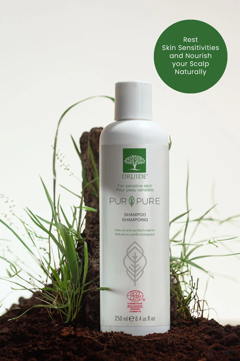 Druide Pur and Pure sensitive skin shampoo flip top dispenser shown in natural environment against mound of fresh soil and green grass with text reading "rest skin sensitivities and nourish your scalp naturally". 