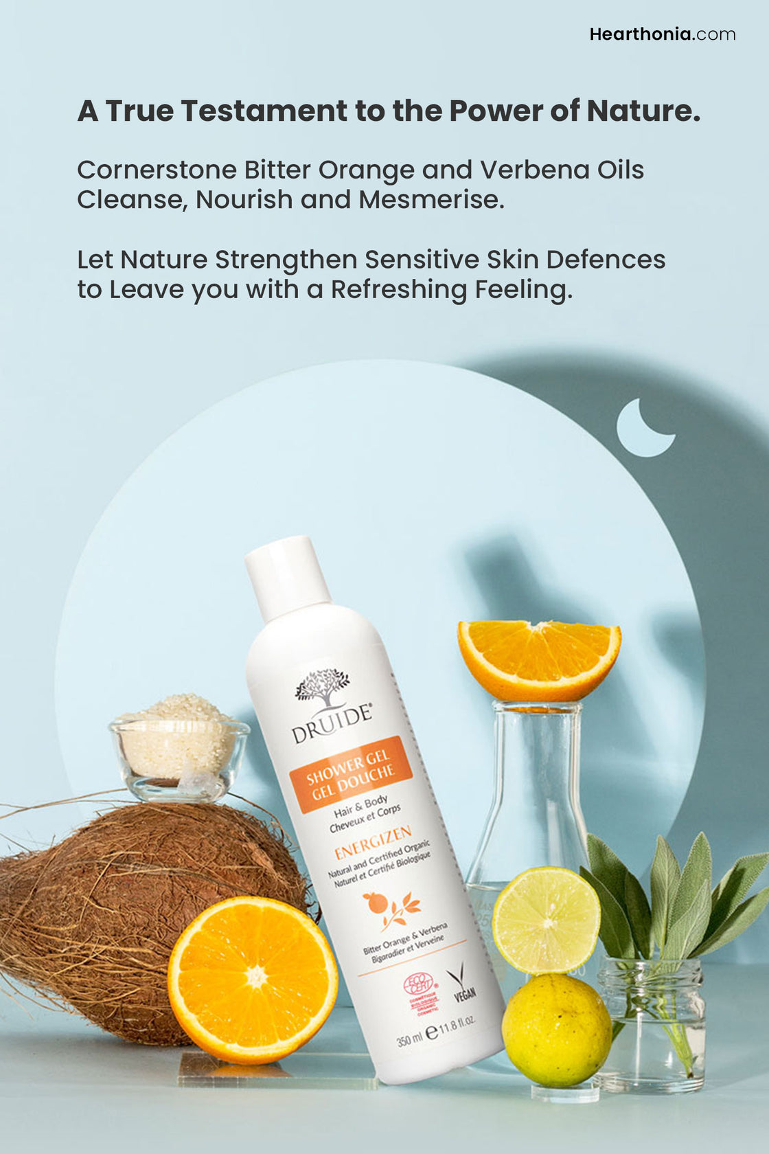 Druide organic hair and body wash   
dispenser leaning on coconut surrounded by pure ingredients like cut lemons and oranges, sage leaves and some refined extracts, highlighting its natural and organic composition with text reading "a true testament to power of nature".