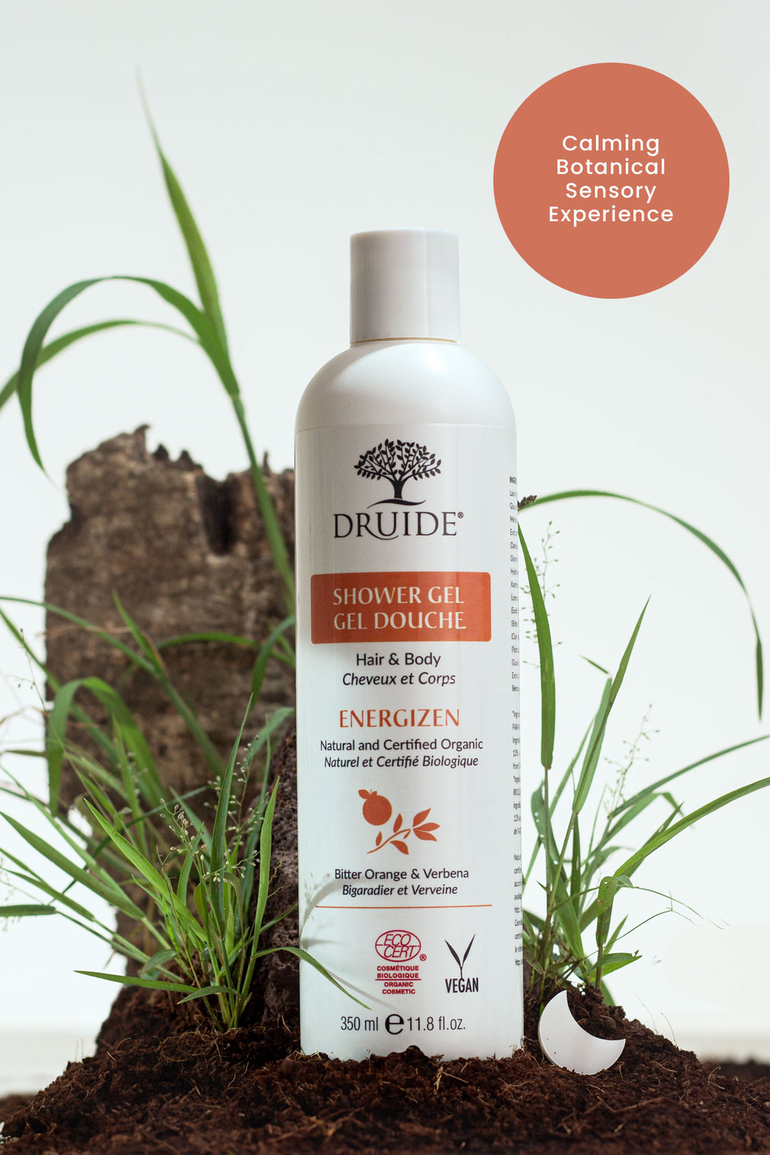 Druide organic hair and body wash   
dispenser in natural environment of fresh soil and green grass with text reading "calming botanical sensory experience".