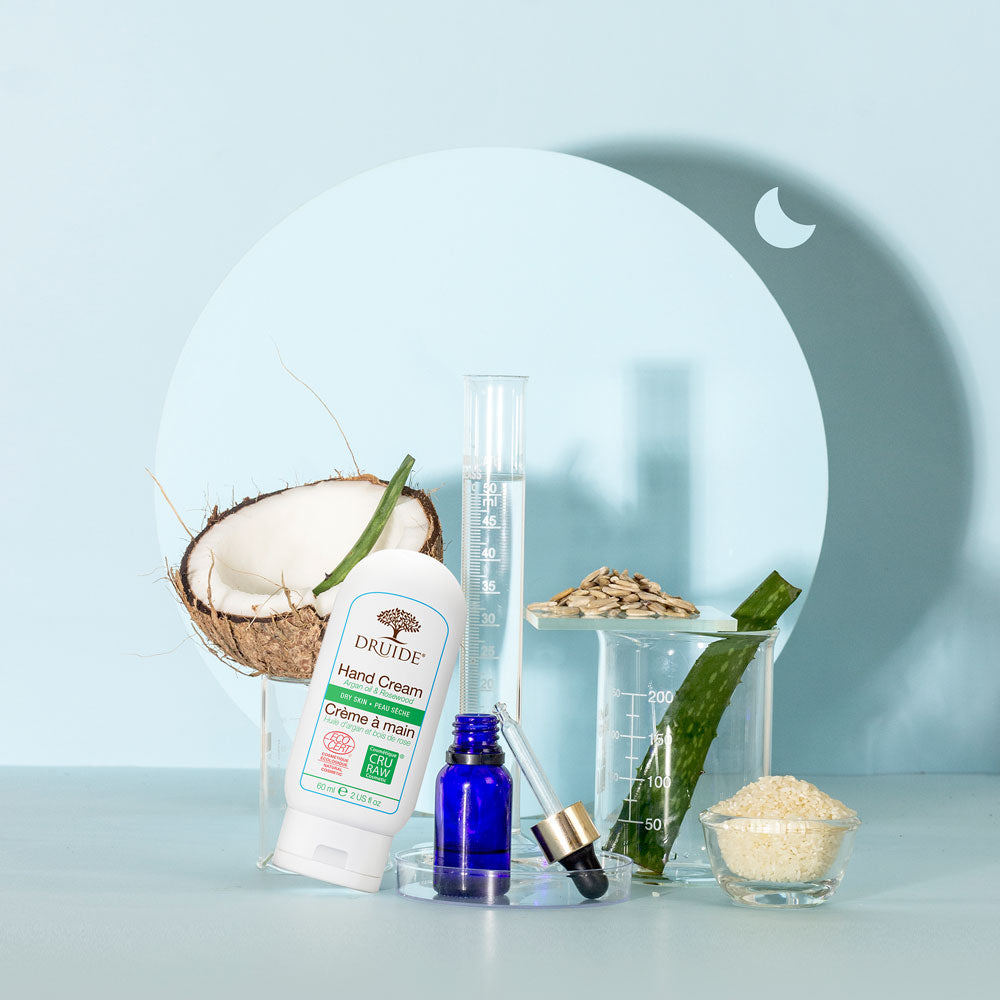 Druide organic Hand Cream for Dry Skin is shown surrounded by lab gadgets and organic ingredients aloe vera, some seeds along with a coconut.